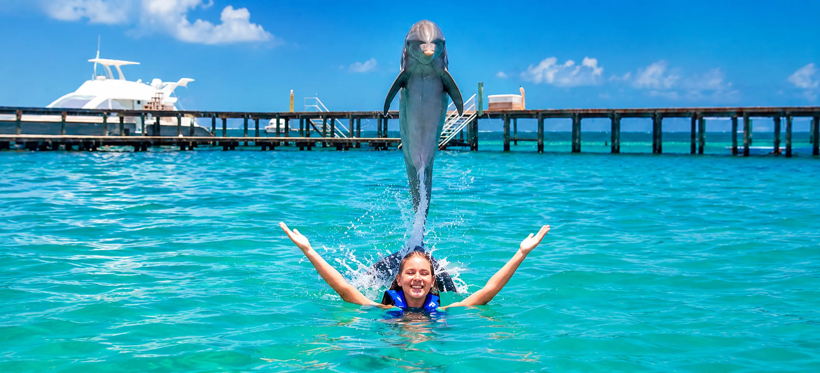 	Guest enjoying the Dolphin Explorer experience in Punta Cana as a dolphin leaps from the crystal-clear Caribbean Sea during an unforgettable swim with dolphins adventure.