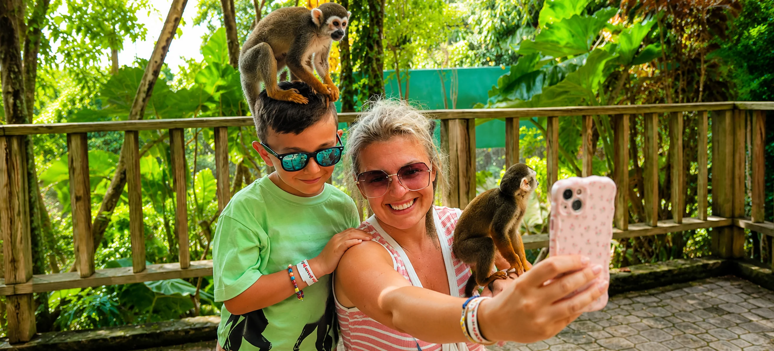 	Three guests laughing as friendly squirrel monkeys climb on their shoulders and feed from their bowls during the Monkeyland Punta Cana family wildlife adventure in the Dominican Republic.