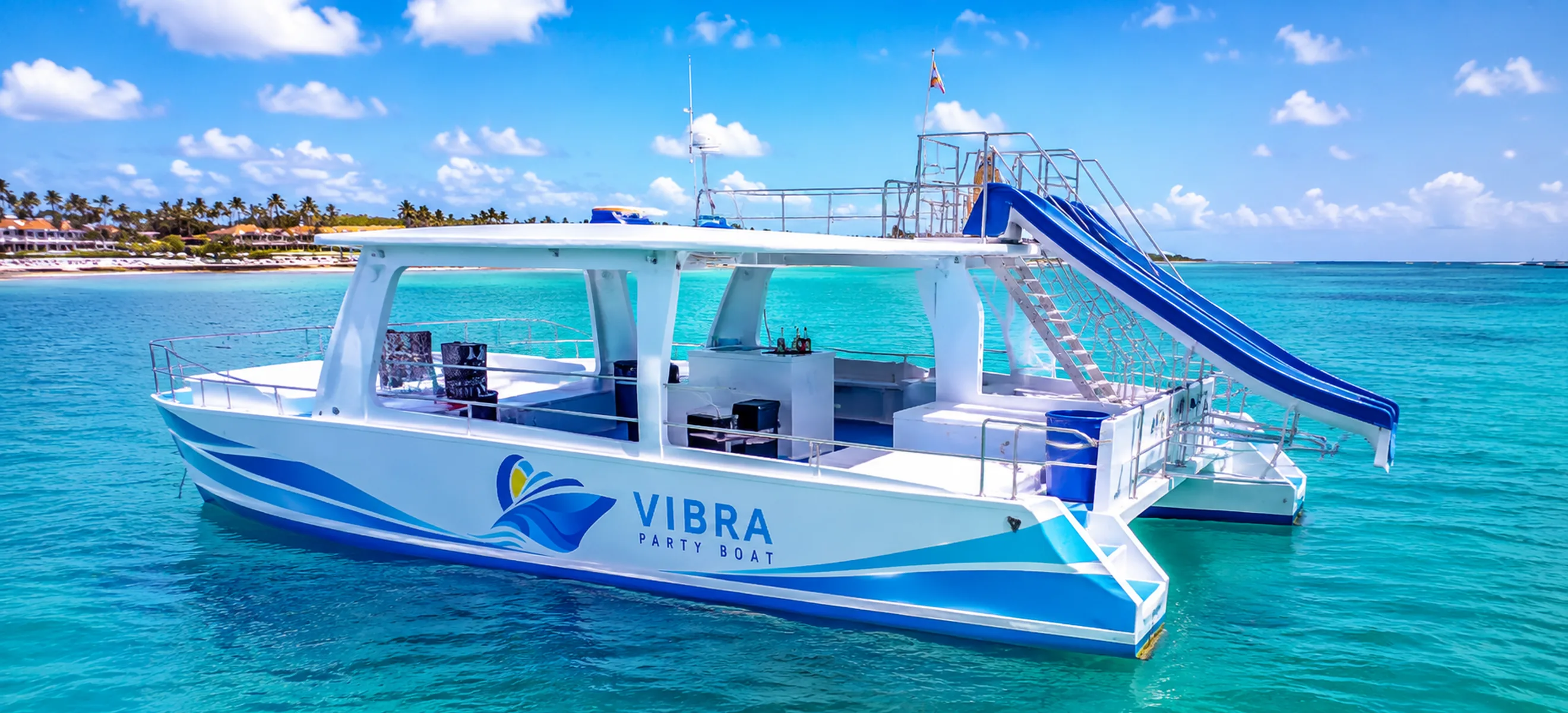 exterior bar area of the Vibra Bávaro Party Boat overlooking the turquoise Caribbean Sea and the palm-lined coastline of Punta Cana.